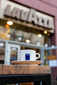 White cup with Lavazza brand logo and saucer on wooden table of Lavazza cafe. Minsk, Belarus - August 14, 2024