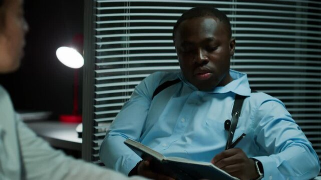 African American male detective talking to female colleague and taking notes during converation in crime lab