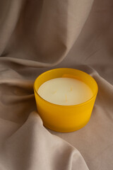 Yellow candle on the wooden table with flax background