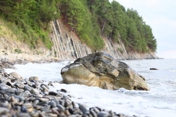 A large rock sits atop a sandy beach, overlooking the vast ocean