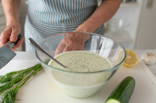 Woman preparing cacik a fresh turkish yogurt sauce with herbs on kitchen counter