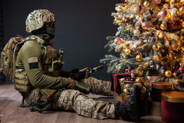 a soldier sits near a Christmas tree. the soldier looks at the Christmas tree