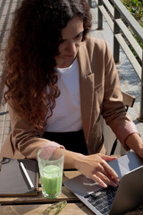Woman working on a laptop outdoors with matcha drink. Remote learning: woman using laptop and sipping matcha.