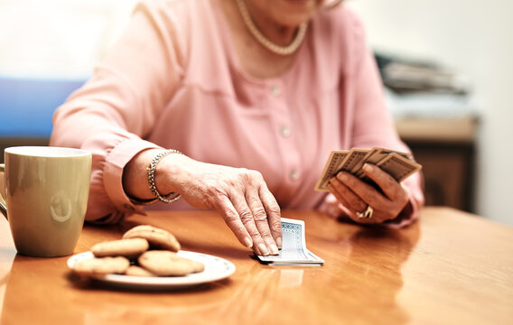 Hands, playing and senior woman with cards in retirement home for poker with cookies and tea. Fun, gambling and elderly female person with rummy game for entertainment at medical nursing facility.