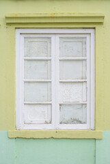 Ventana blanca cerrada en fachada amarilla y verde