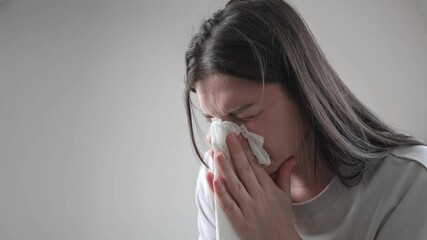 Young brunette woman closes her eyes and blows her nose, dealing with nasal congestion from seasonal allergies. - Powered by Adobe