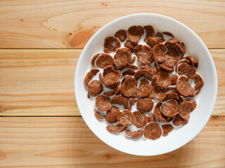 Chocolate breakfast cereal in a white bowl on wooden table