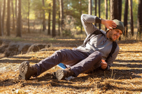 Young man having trouble feeling knee pain during travel in forest. Health problem in journey, copy space