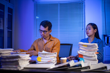 Image of businessman working hard in front of many documents on desk at office late at night with serious action. Concept of working hard and too late.