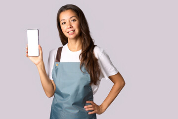 Happy woman wearing apron showing the smartphone white screen, shopping concept