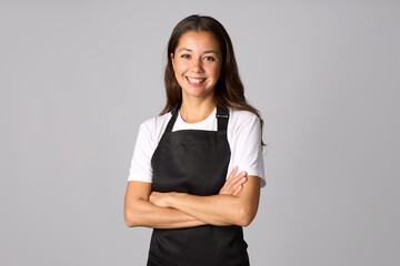 Portrait of young woman in black apron standing with arms crossed. Woman wearing apron and white shirt, white background