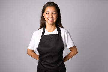 Friendly waitress, female barista in black apron. Young woman wearing black apron and white shirt standing on a white background with copy space