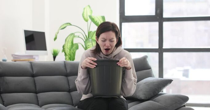 Woman holding bucket and vomiting at home