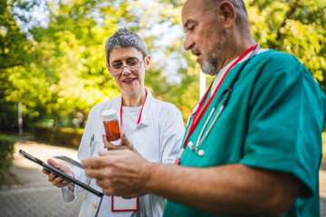 Two healthcare professionals review tablet outdoor in uniforms