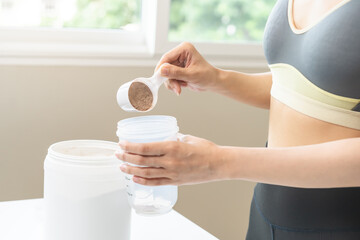 Diet meal replacement for weight loss, asian young woman in sportswear, hand in holding scoop making protein into bottle to shake, drink supplement for muscle after workout at home. Healthy body care.