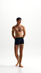 Fototapeta premium Full-length portrait of handsome young man with relief, muscular body, posing in black boxers isolated on white studio background. Concept of male beauty, body and skin care, health, sport