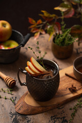 Apple Moscow Mule cocktail in a copper mug on a wooden rustic background. Autumnal Spiced Cider with honey, apple slices, thyme and cinnamon stick as a garnish. Cozy autumn evening. Drink photography