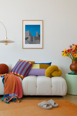 Bright and cozy living room with a modern white sofa adorned with colorful cushions and throw blankets. Vibrant flowers and geometric wall art complete the lively, welcoming atmosphere. © FollowTheFlow