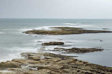 Long exposure of granite stone pier seawall and rocks along coast coastline in England, uk,...
