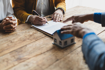 The real estate agent is explaining the terms of the home purchase agreement contract and the client legally signs the contract. Couple is signing a home sales contract with the salesman.