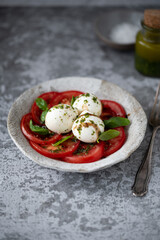 Italian caprese salad with sliced tomatoes, mini mozzarella balls, basil, olive oil and balsamic vinegar. Healthy food concept. Italian cuisine.