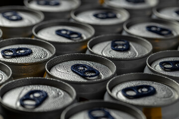Close-up of aluminum beverage cans covered in condensation. The cans are arranged in rows, featuring dark blue pull tabs, with water droplets emphasizing the coldness and freshness