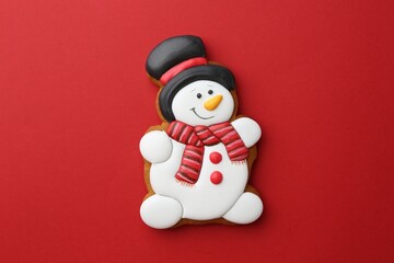 Tasty Christmas cookie in shape of snowman on red background, top view