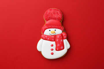 Tasty Christmas cookie in shape of snowman on red background, top view