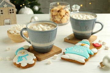 Delicious cookies in shape of snowmen, cups with cocoa and Christmas decor on white wooden table