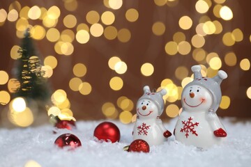 Funny snowman figure and other Christmas decor on artificial snow against blurred lights