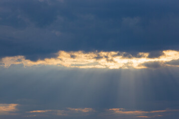 Golden rays of the sun make their way through blue heavy cumulus clouds as transparent pillars of light. Sunbeams break through a clouds. Holy Light comes from heaven