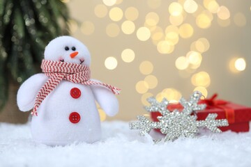 Funny snowman figure and decorative snowflake on artificial snow against blurred lights