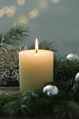 Burning candle, baubles and fir tree branches on wooden table, closeup