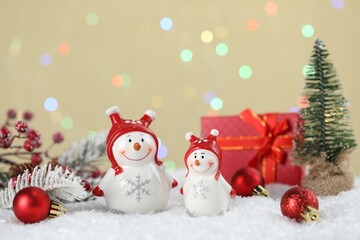Cute snowmen and other Christmas decor against beige background with blurred lights, bokeh effect
