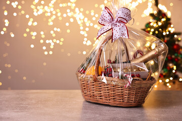Wicker gift basket with sparkling wine and Christmas decor on light grey textured table, space for text