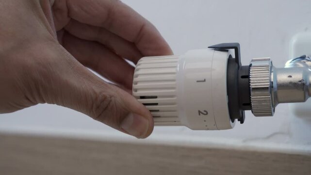 Close up of a white thermostatic valve being adjusted to a lower setting to reduce heat and save money. Could be reversed to increase the heat. Zoom in.