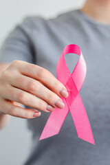 Woman in gray t-shirt holds pink ribbon in her hands. Breast Cancer Awareness Month. Supporting and...