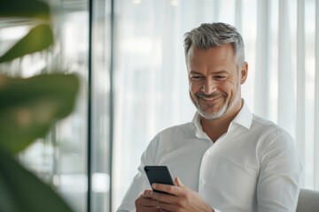 Fototapeta premium Mature man smiling while using smartphone in modern office