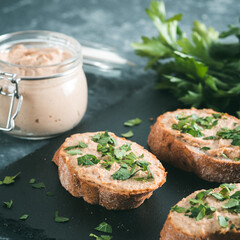 Close up view of slice bread with homemade turkey pate and fresh green parsley on black slate board over gray concrete background, Copy space. Shallow DOF
