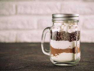 Hot chocolate mix in mason jar. Homemade mix from cocoa, dry milk, sugar, chocolate chips and marshmallows. Christmas and winter holiday budget-friendly holiday gifts idea. Copy space. Toned image