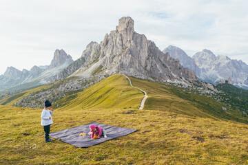 Naklejka premium Children Playing Outdoors on a Picnic Blanket in the Dolomites, Two young children playing on a picnic blanket in the Dolomites, surrounded by majestic mountain scenery and open nature.