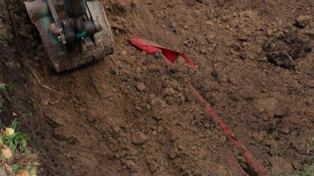 A mini digger is actively engaged in excavating soil in a residential backyard, preparing the area for landscaping improvements. The machine removes dirt and debris, showcasing efficient digging techn