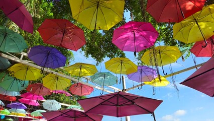 Bottom view of colorful umbrellas hanging in the sky, decorated colored umbrellas in coffee shop on street. Vivid colorful umbrellas sweep overhead string in the wind.