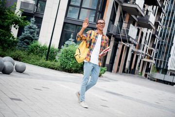 Full length portrait of nice young man walk wave hi wear plaid shirt buildings downtown street outdoors