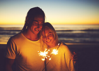 Couple, romance and sparkler on beach at night for new year celebration, party event and hug on holiday. Tourist, people and fireworks at ocean sunset for vacation, travel and embrace with affection
