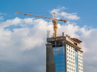 Equipment for the construction and lifting of bulky goods with construction materials. A tower crane in the clouds towers over a high-rise building under construction. Construction equipment.