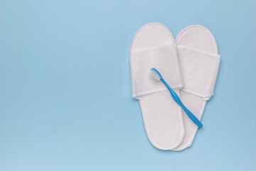 White Hotel Slippers and Blue Toothbrush on Light Blue Background