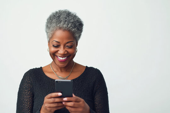 Mature woman is smiling while looking at her smartphone against a white background