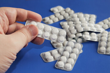hand holding a blister of white tablets on a blue background with similar pills, white pills on a...