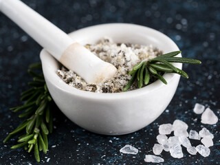 Close up view of mortar and pestle with sea salt scented rosemary and lemon zest. Sea salt scented herb rosemary on dark blue background. Scented salt and ingerdients. Copy space
